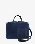 Introducing the Claude by Clare Vivier: a chic Italian suede laptop bag in dark blue, featuring a black adjustable shoulder strap, top handle, and front pocket. This minimalist bag is designed to accommodate a 13-inch laptop and is presented against a clean white background.