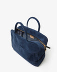 The Claude by Clare Vivier is a navy blue Italian suede handbag with two handles and a gold zipper. It features a front pocket and a partially open top, revealing a gray interior. Perfect for chic outings, this versatile bag is set against a plain white background.