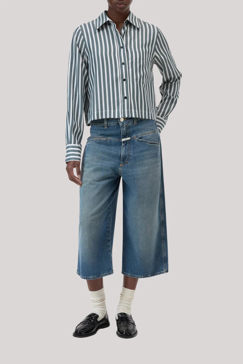 A person wearing the CLOSED Cropped Classic Shirt in gray and white stripes, knee-length wide-leg denim shorts, white socks, and black loafers stands against a plain light gray background.