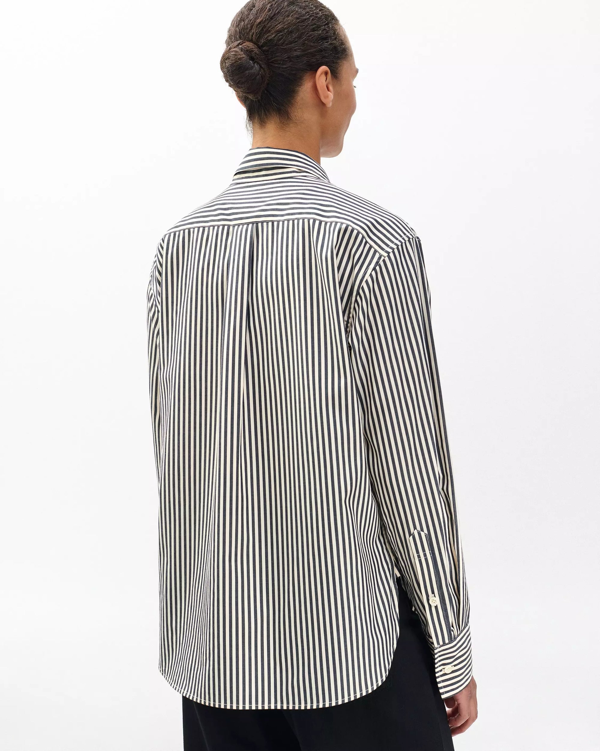 A person with dark hair in a bun is seen from behind wearing the Rag & Bone connie striped shirt—black and white vertical stripes—paired with black pants, set against a plain white background.
