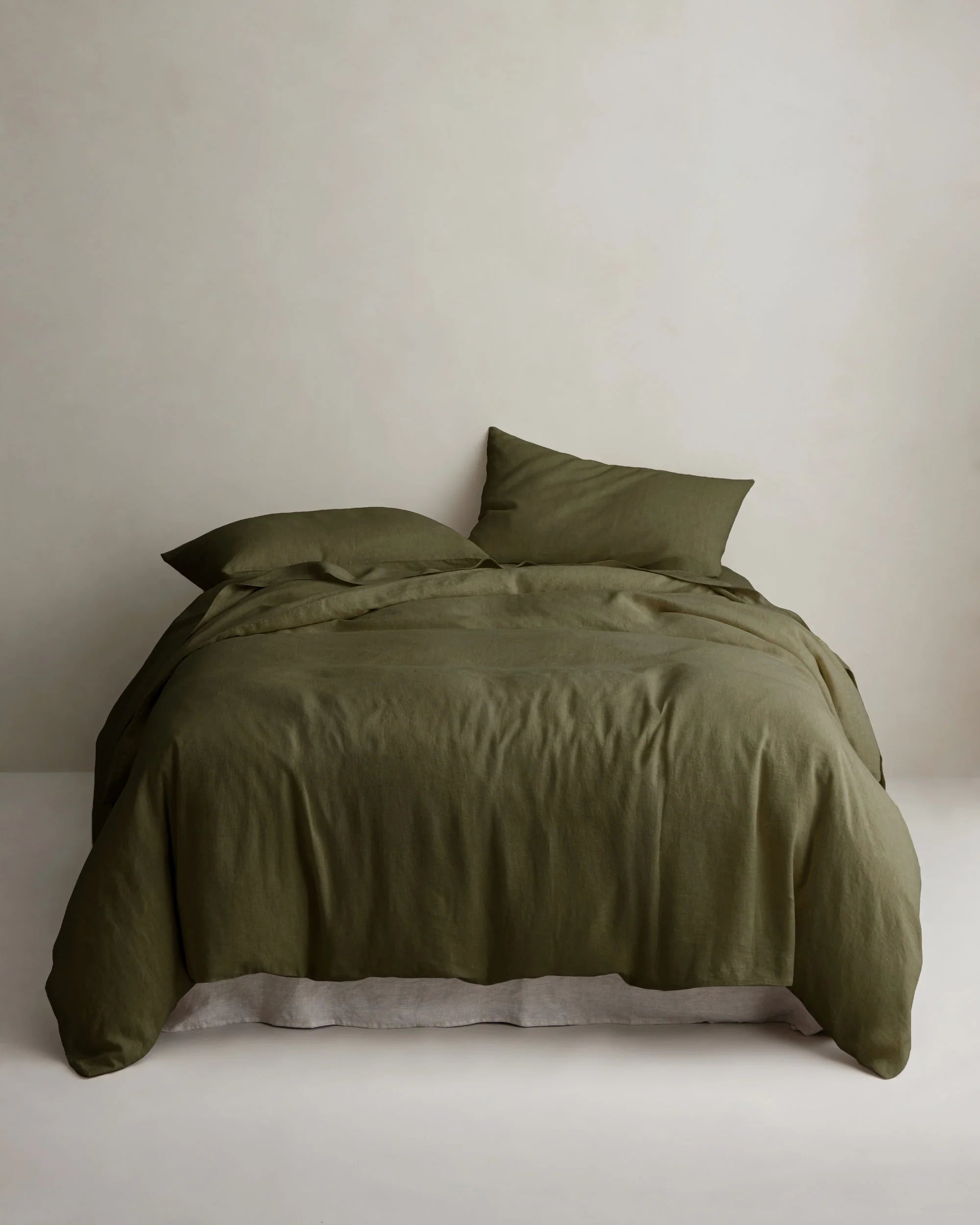 Olive green linen duvet cover by Cultiver Goods on a neatly made bed with two pillows against a light wall.