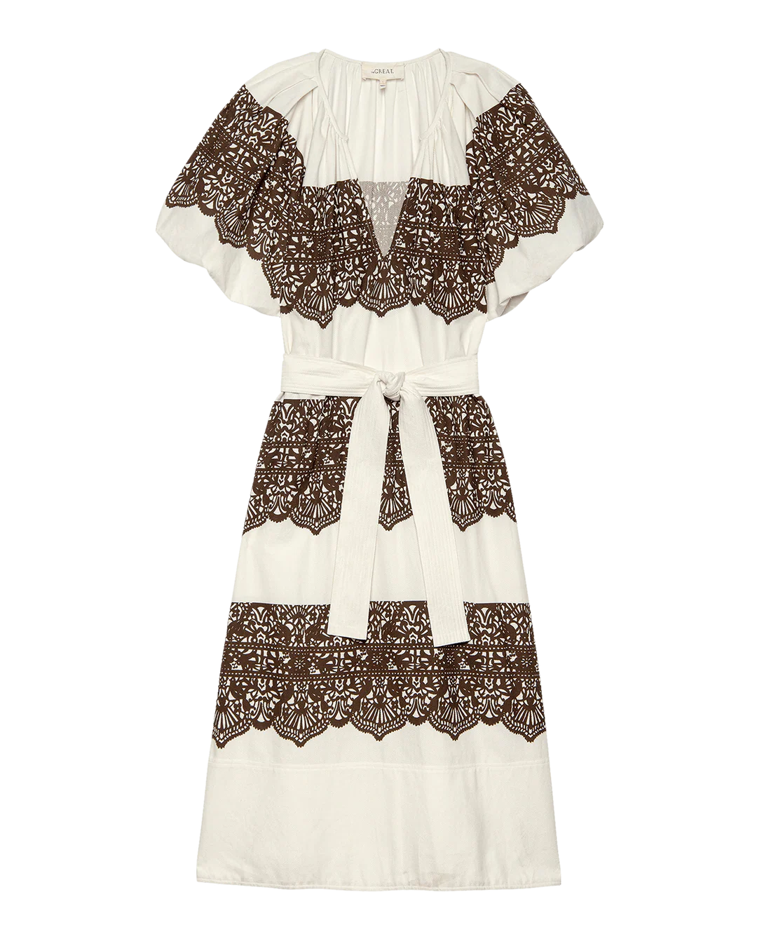 The Fairground Dress by The Great Inc. is a white knee-length style with short sleeves, wide horizontal western lace print bands, and a matching fabric belt at the waist.