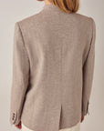 A person with long blonde hair is seen from behind wearing the Maison Hotel Nehru Jacket in light beige and perforated white pants, inspired by Indian tailoring, against a plain light-colored background.