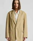 Deconstructed blazer with belt by Denimist, layered over a striped shirt and blue jeans against plain background.