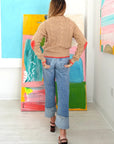 Kerri Rosenthal Maxwork Cable Sweater in a colorful art-filled room, styled with cuffed jeans for a casual look.
