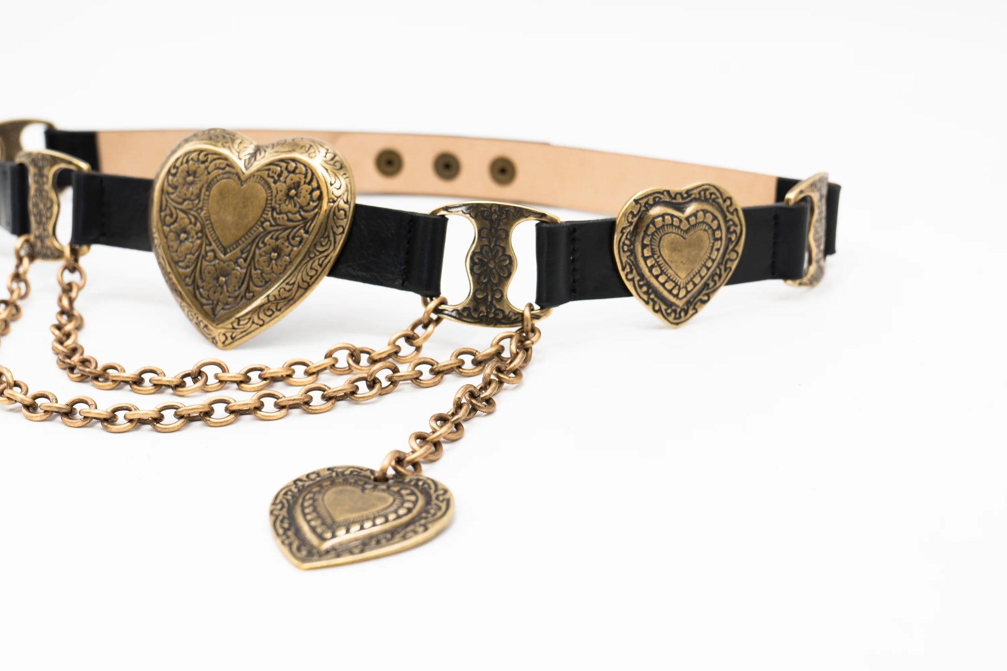 The Brass XL Heart Belt by Streets Ahead Inc is a black leather belt with ornate Italian brass heart-shaped buckles and decorative chains, featuring detailed etchings, handcrafted in Los Angeles and shown on a white background.