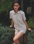 A dark-haired woman stands outdoors by a fence amid green foliage, wearing the Ines De LA Fressange Nicia Shirt and matching shorts.