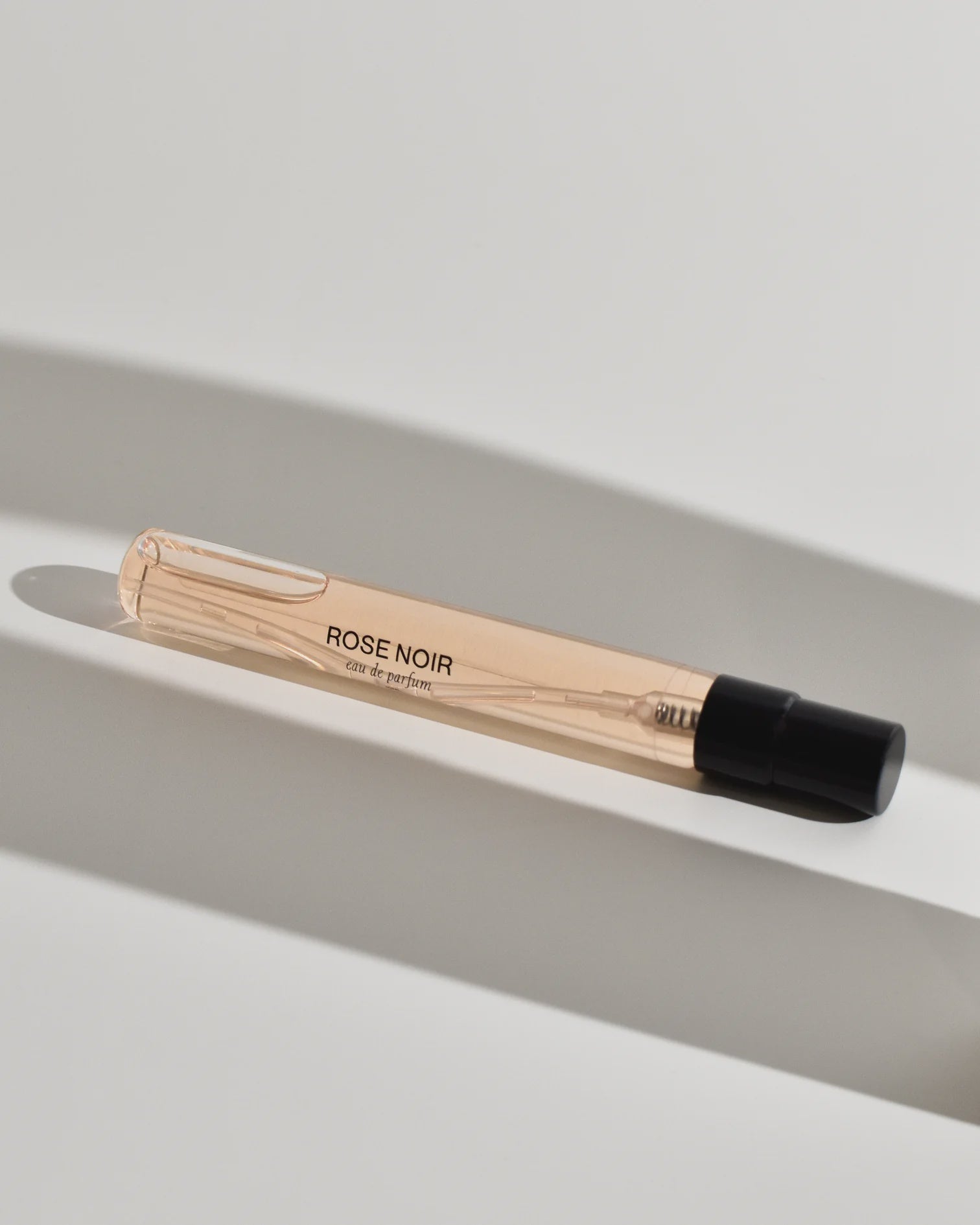A small, transparent vial labeled "Rose Noir parfum" by SOL E'CIEL with a black cap rests on a white surface, suggesting the floral and spicy notes of this fragrance.