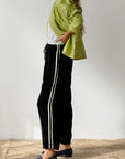 In a profile pose against a plain backdrop, someone wears The Velvet Stripe Crop by Donni with a green jacket and white shirt. Relaxed fit pants are paired with dark slip-on shoes, hand in pocket, showcasing casual elegance.