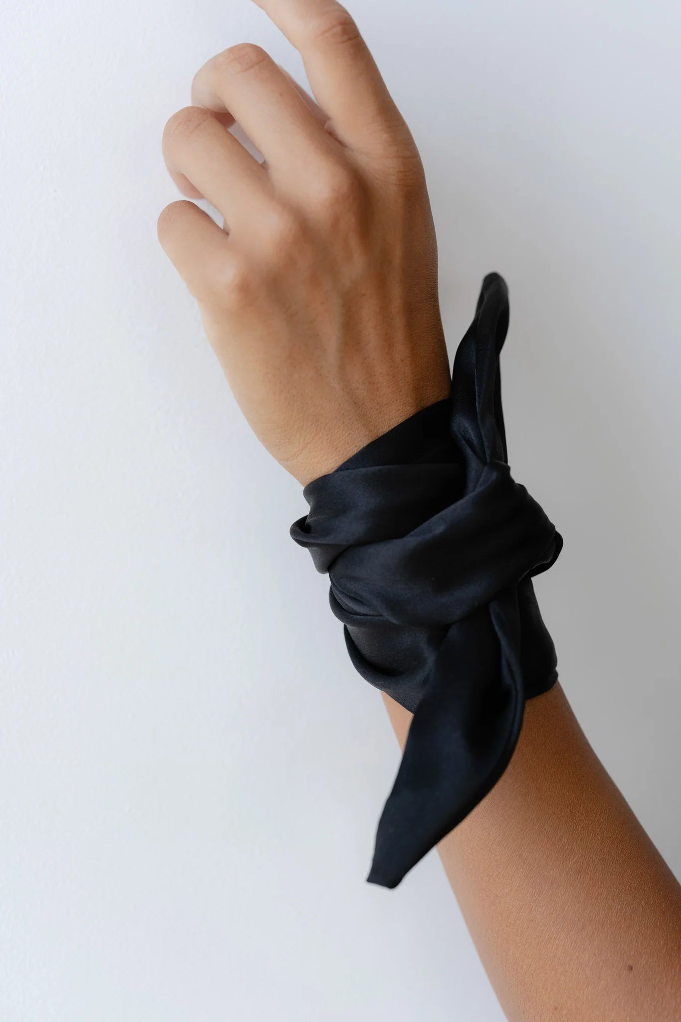 A hand against a white background is adorned with an elegant accessory from Donni: The Silk Bow, crafted from 100% black silk and tied gracefully around the wrist.