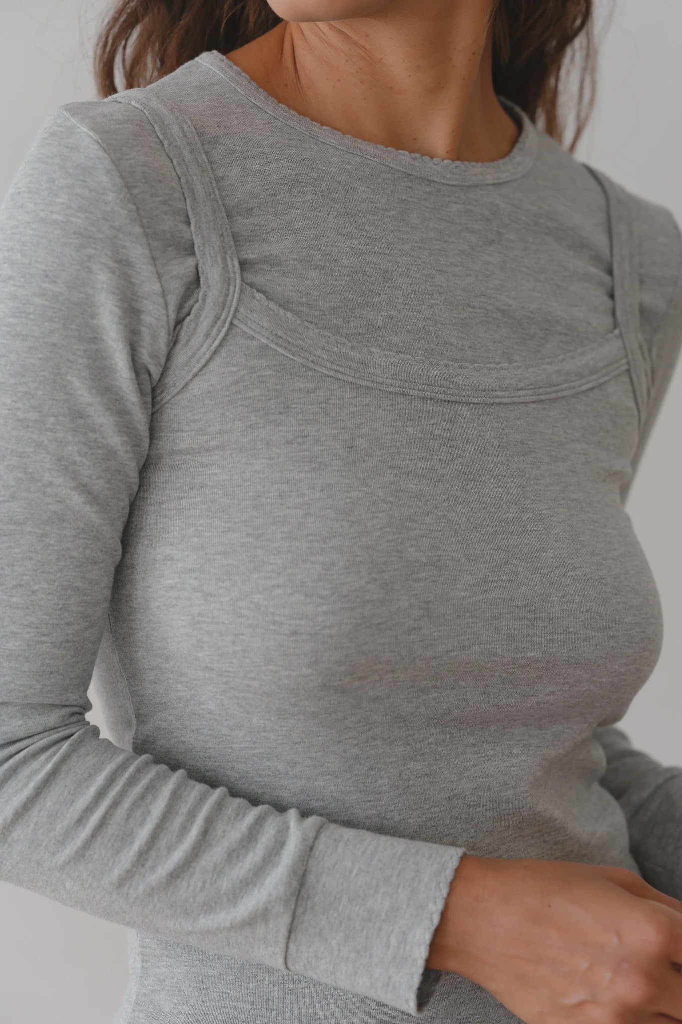 A person models The Baby Rib Long Sleeve from Donni in gray, featuring visible seam details and highlighting the Baby Rib Scallop texture against a neutral background, with the focus on the upper body and outfit.