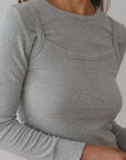 A person models The Baby Rib Long Sleeve from Donni in gray, featuring visible seam details and highlighting the Baby Rib Scallop texture against a neutral background, with the focus on the upper body and outfit.