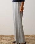 A person stands on a textured floor, clad in black long-sleeve shirt and The Baby Rib Scallop Pant by Donni in gray, along with brown sandals. The image is cropped to display only the lower half of the body.