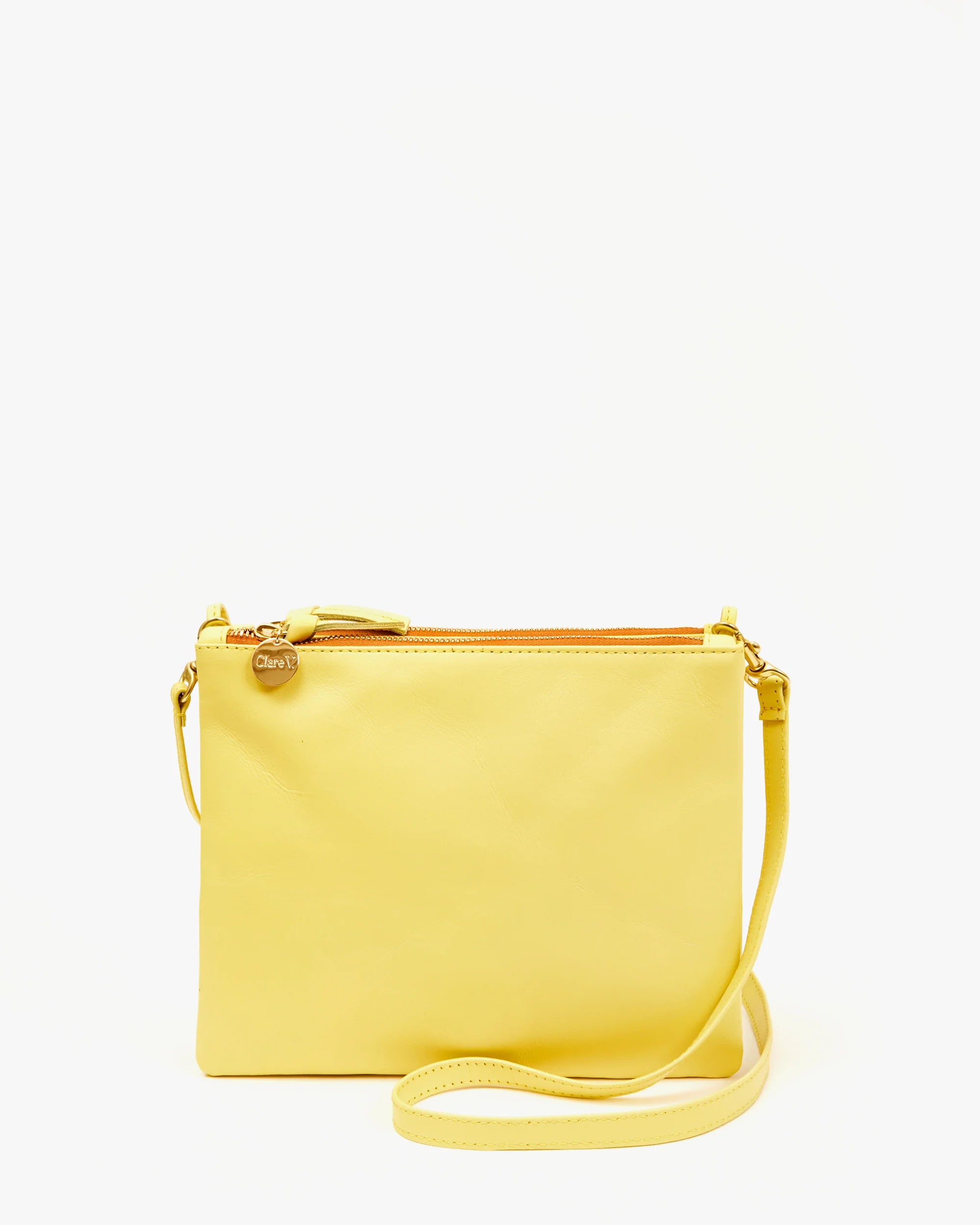 The Double Sac Bretelle by Clare Vivier is a yellow Italian leather crossbody bag with a slim design, featuring a top zipper closure, zippered pouches, a detachable shoulder strap, and a small metal tag near the zipper. The bag is set against a plain white background.