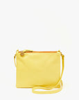 The Double Sac Bretelle by Clare Vivier is a yellow Italian leather crossbody bag with a slim design, featuring a top zipper closure, zippered pouches, a detachable shoulder strap, and a small metal tag near the zipper. The bag is set against a plain white background.