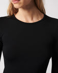 A woman with light skin and long blonde hair models the Majestic Filatures Soft Touch L/S Crewneck T-Shirt in black. Cropped from shoulders to chest, the image highlights this fitted, comfortable tee against a plain light background.