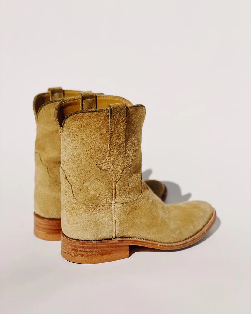 A pair of The Ranch Boot by Hey Gang, crafted from light brown calf skin suede, featuring wooden heels and displayed on a plain white background. These roper-style boots are slightly angled to highlight their back and side details.