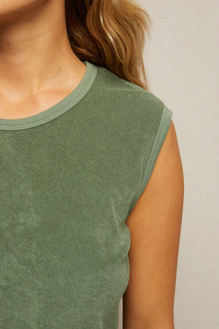 Close-up of a person wearing the ELLIE terry banded tank by Perfectwhitetee in sage green, featuring a ribbed neckline. Their wavy, light brown hair is over one shoulder, with a plain light background and face partially out of frame.