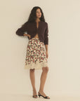 DOEN Elowette Skirt in brown paired with a matching cardigan and black heels, styled against a neutral wall.