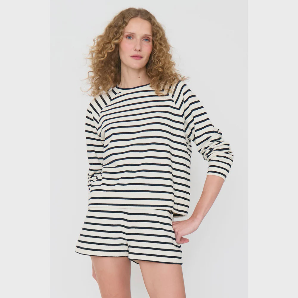 A person with curly hair models The Eco Cotton Franny by Kule, featuring a long-sleeve, black and white striped top paired with matching shorts, set against a plain white background. They stand with one hand on their hip and have a neutral expression.