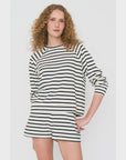 A person with curly hair models The Eco Cotton Franny by Kule, featuring a long-sleeve, black and white striped top paired with matching shorts, set against a plain white background. They stand with one hand on their hip and have a neutral expression.