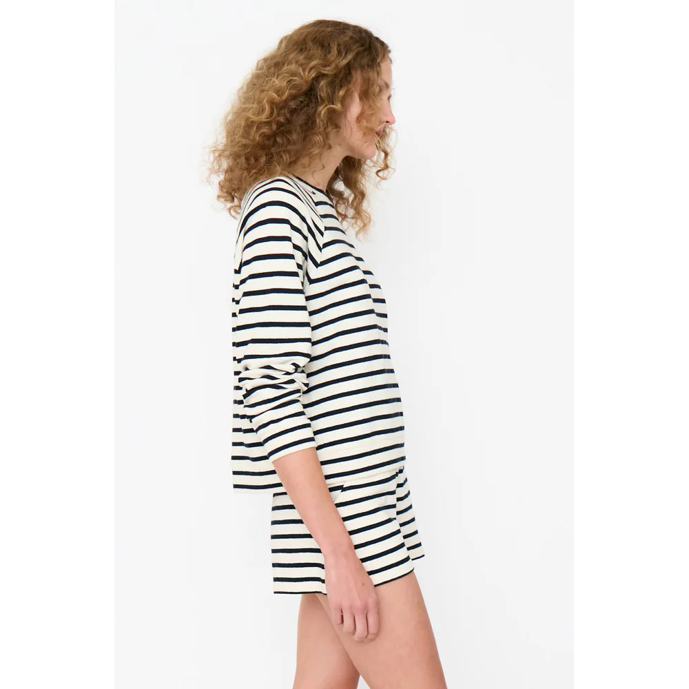 A person with curly hair is shown in side profile wearing Kule's The Eco Cotton Franny, a striped long-sleeve top and shorts. Crafted from midweight cotton slub jersey, the black and white horizontal stripes offer a simple yet casual vibe against the plain background.