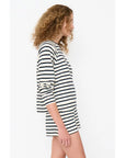 A person with curly hair is shown in side profile wearing Kule's The Eco Cotton Franny, a striped long-sleeve top and shorts. Crafted from midweight cotton slub jersey, the black and white horizontal stripes offer a simple yet casual vibe against the plain background.