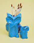 Blue Serax Owl vases on a yellow surface, one used as a paintbrush holder; playful ceramic decor for Bungalow.