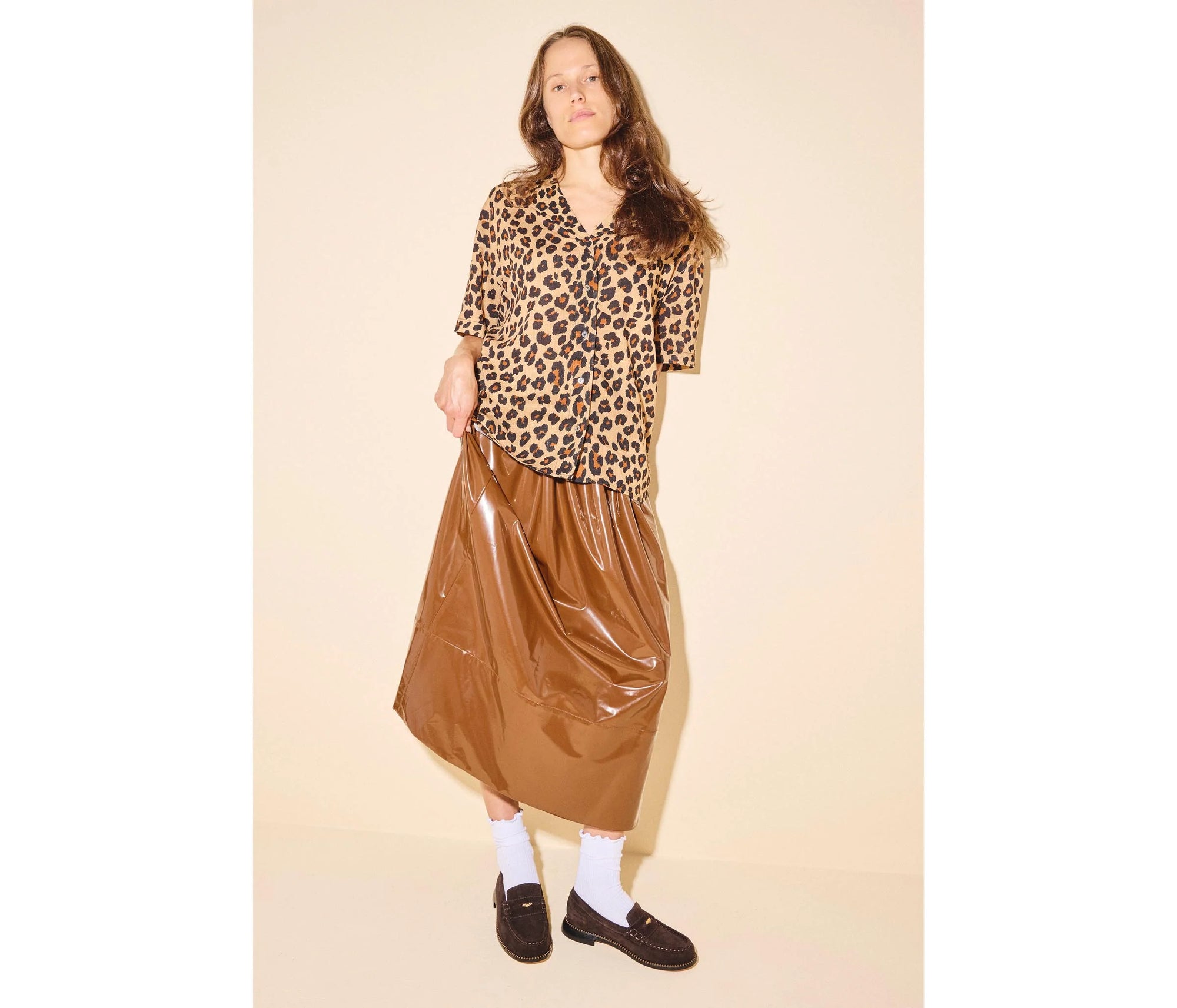 A woman with long brown hair and a relaxed pose wears a leopard print blouse, shiny brown midi skirt, white socks, and the Freda Salvador Elba Espresso Suede Loafer against a plain background.