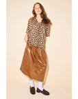 A woman with long brown hair and a relaxed pose wears a leopard print blouse, shiny brown midi skirt, white socks, and the Freda Salvador Elba Espresso Suede Loafer against a plain background.