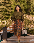 Eli Top by Hunter Bell NYC styled with a skirt and tote on a dock, boats and trees in the background.