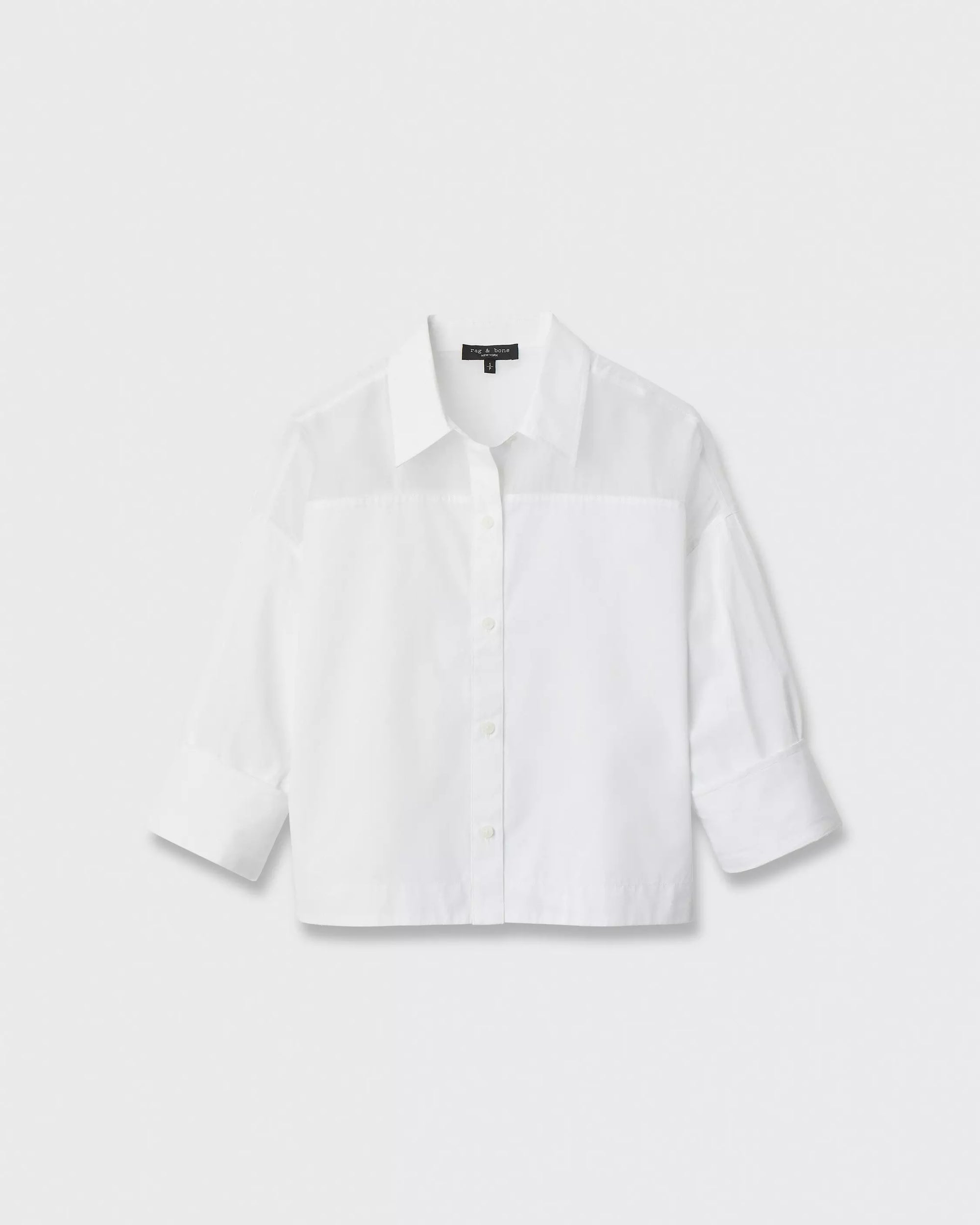 The elly ss shirt by Rag & Bone is a plain white, long-sleeve cropped boxy shirt in cotton poplin, featuring a button front and collar with slightly rolled-up sleeves for a relaxed style, shown on a white background.