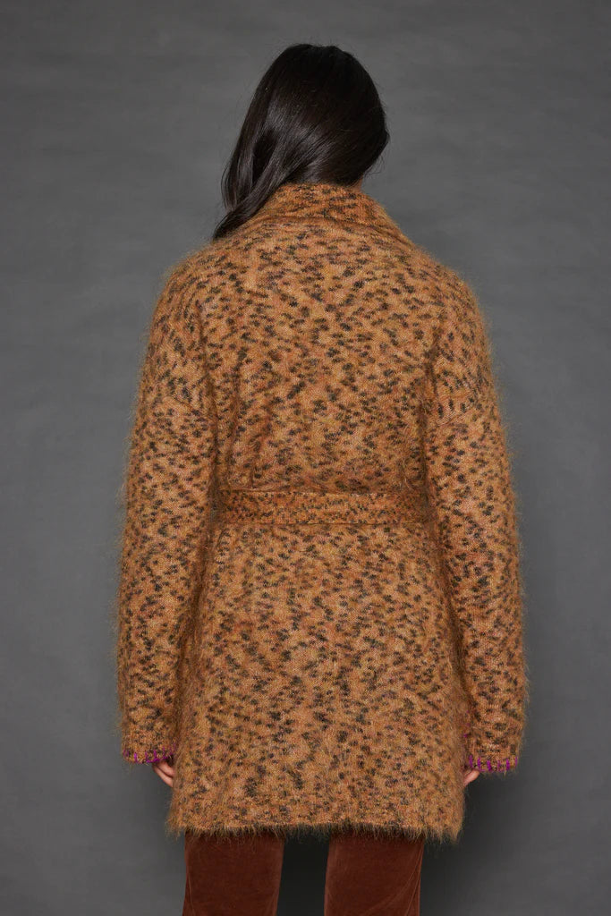 A person with long dark hair is wearing the Lisa Todd Mohair Limited Edition, a luxurious leopard-print coat crafted from fine Italian yarn, over maroon pants. They stand against a plain gray background, facing away from the camera.