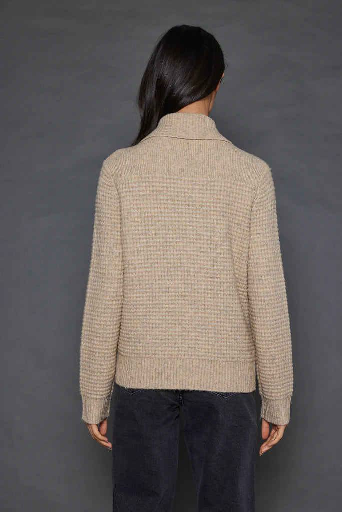 A person with long dark hair is wearing the Deep Pockets Zip sweater by Lisa Todd and dark pants, standing with their back to the camera against a gray background.