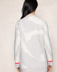 A person with long black hair is wearing the Camo Cloud, a light gray oversized cardigan by Lisa Todd, which features abstract white patterns and bright pink accents on the cuffs. The contrast striping elevates its uniqueness as they face away, creating a perfect pairing with blue jeans.