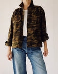 A person models The Work Shirt by Hey Gang—a boxy fit camouflage jacket styled over a white shirt and blue jeans—standing against a plain light background with their face not shown.