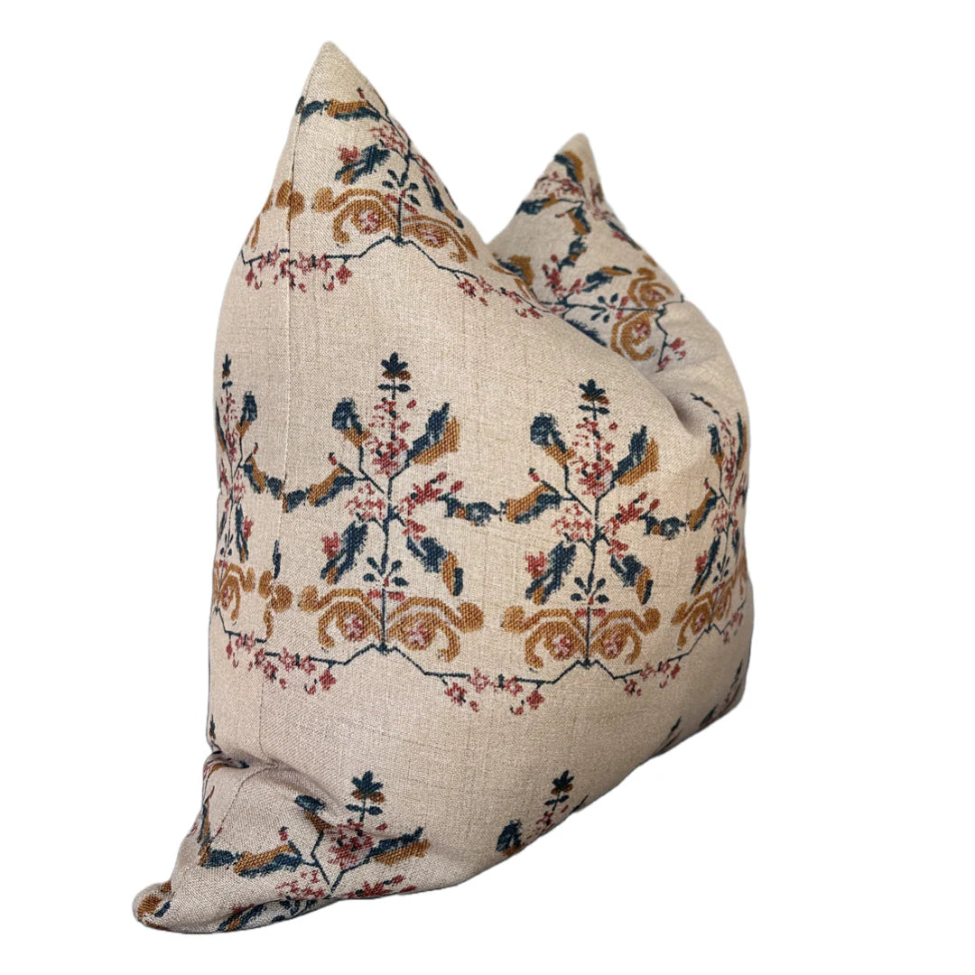 The Rennah Collective Birdie Pillow 22x22 features a beige background with an intricate floral design in blue, gold, and red on a soft woven cover, displayed against a white backdrop.
