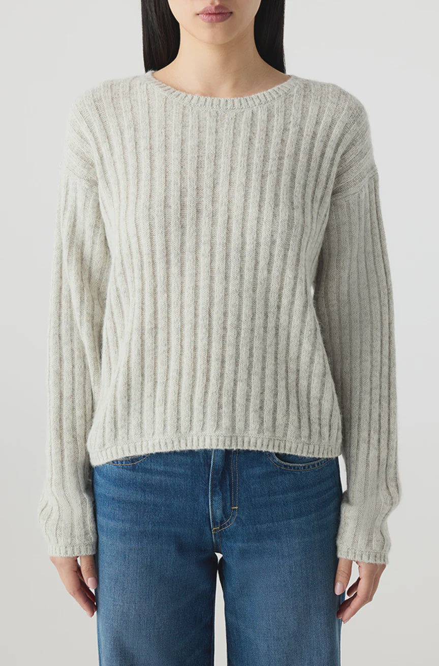 A woman wears the AMO Denim Hallie Sweater, a relaxed boxy knit in light gray alpaca wool with a ribbed crew neck, paired with blue jeans. She stands against a plain light background; the image is cropped above her head and at her thighs.