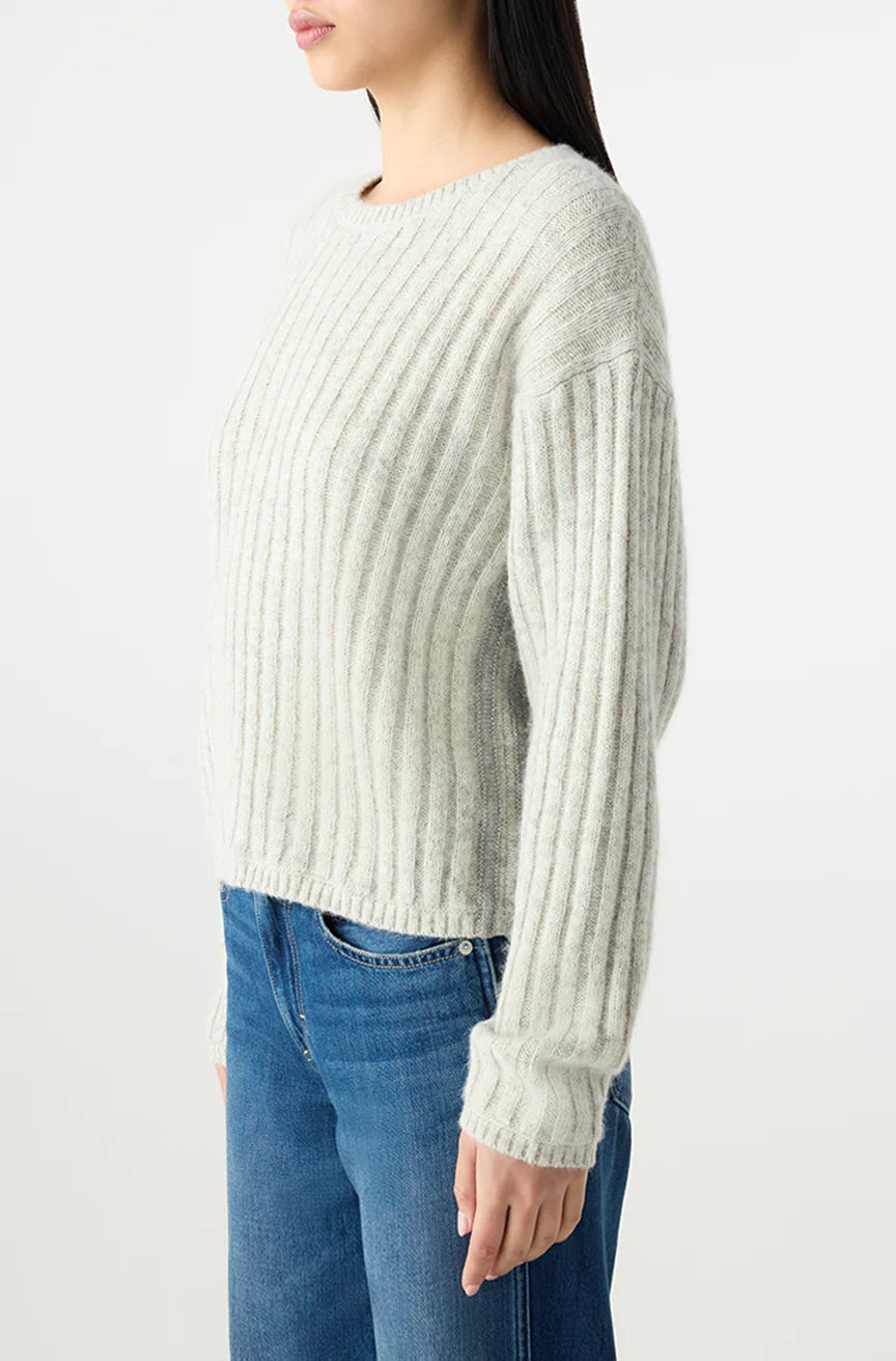 A person, shown from the side against a plain light background, wears the AMO Denim Hallie Sweater in light gray with a ribbed crew neck and long sleeves, paired with blue jeans.