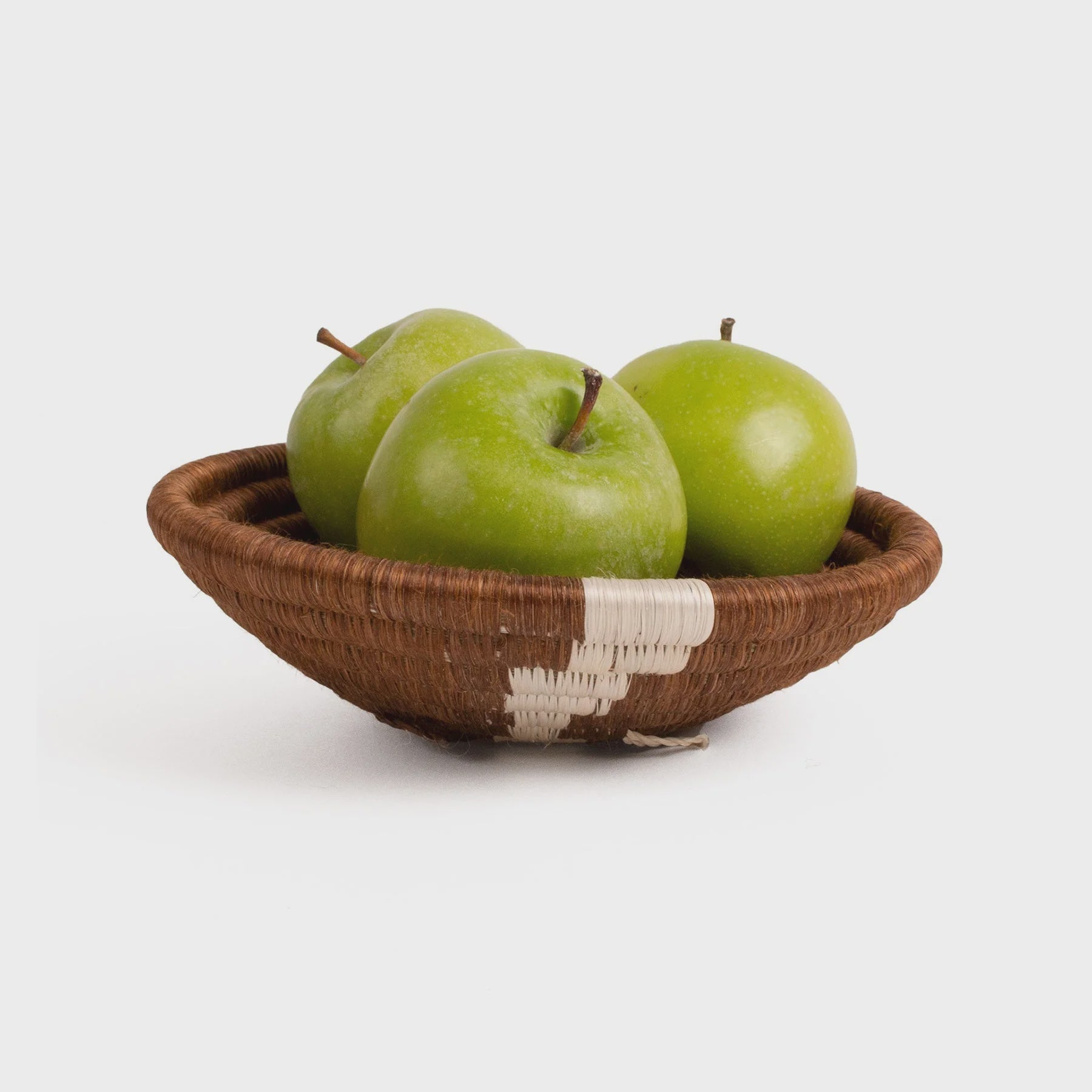 Three fresh green apples in a small brown Woven Bowl 6&quot; by Kazi Goods against a white background in a Scottsdale, Arizona Bungalow.