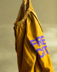 A pair of Flap/Snap LG MATTE/SATIN AirJump Pants in mustard-yellow, adorned with a purple "FREE CITY" logo on an elastic waistband, featuring a custom sunfade wash, set against a yellow-green background. 

Brand: Free City (sparrow, LLC)