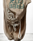 A pair of Flap/Snap LG MATTE/SATIN AirJump Pants by Free City (sparrow, LLC), featuring tan drawstring design with an upside-down "FREE CITY" and blue bird graphic in custom sunfade wash, displayed on white; freecitysupershop logo below.