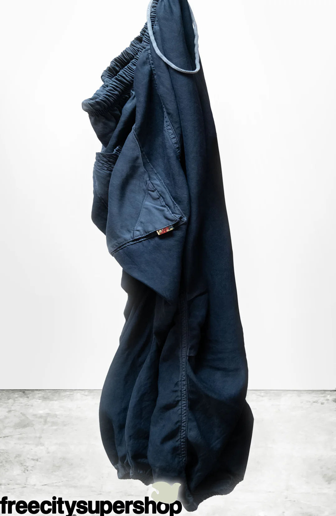The Loose Drawcord Biggy Pant by Free City (sparrow, LLC) in dark blue hangs against a plain white background, with the "freecitysupershop" logo in black at the bottom left corner.