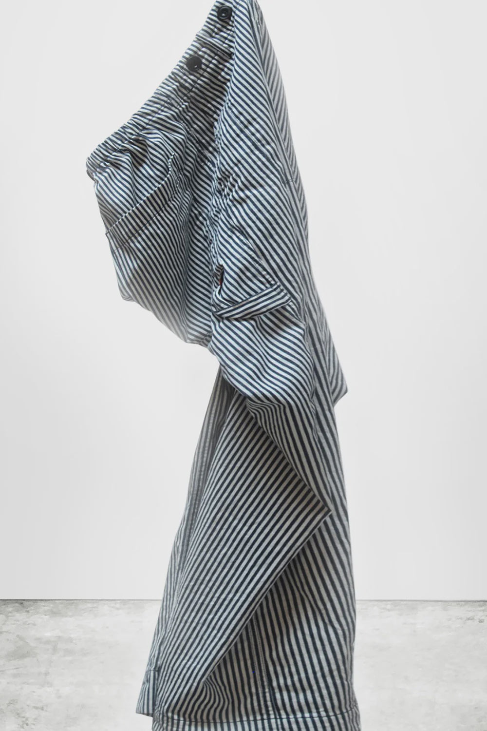 The Indigo Stripe Sailor Pant by Free City (sparrow, LLC) stands upright, partially folded with bent legs and uneven sides, set against a plain white background and concrete floor.