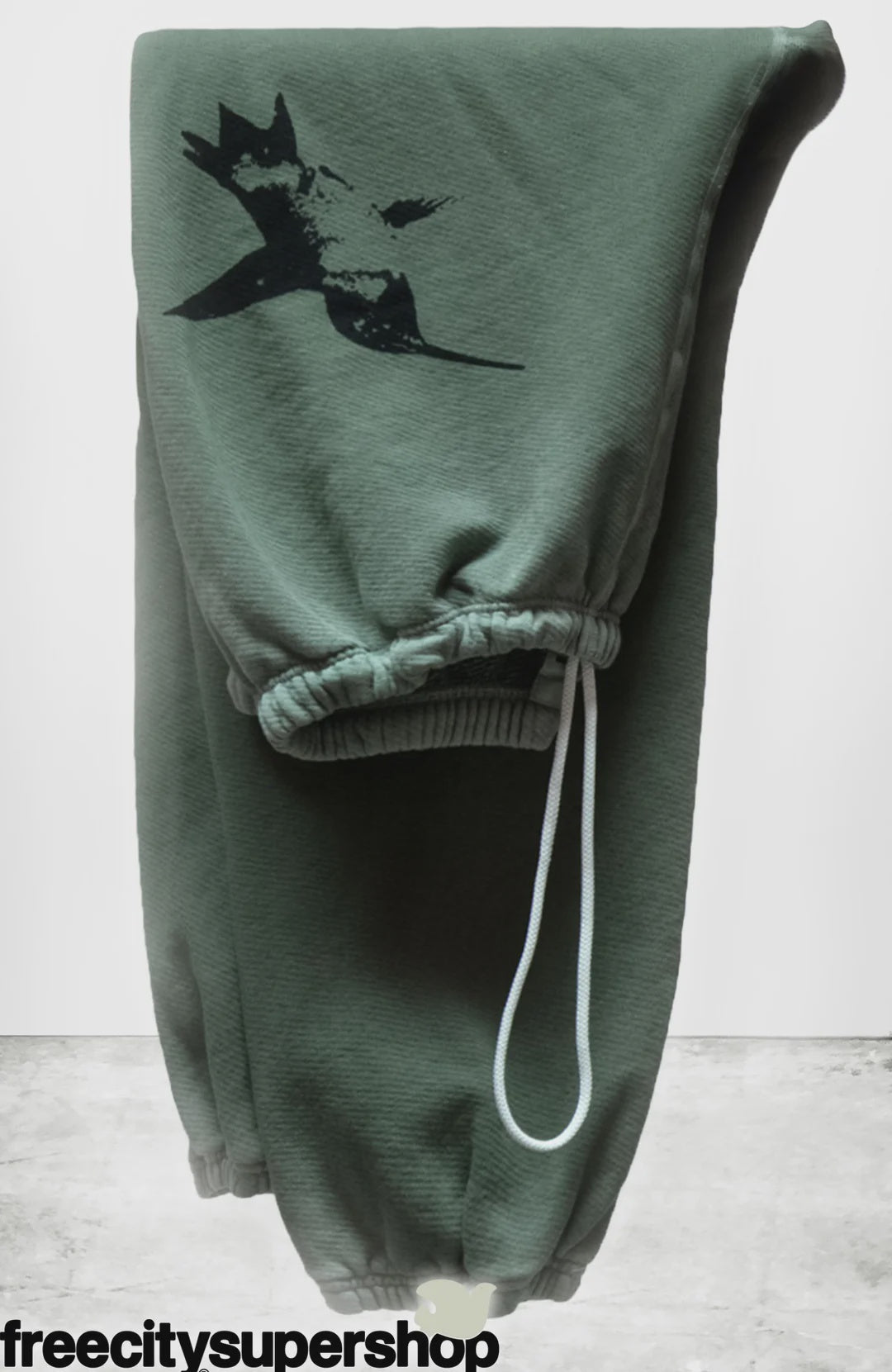 Super Vintage Yumm OG Sweatpant by Free City (sparrow, LLC): green unisex French terry sweatpants with a black bird graphic on the thigh, white drawstring, and elastic cuffs, shown on a neutral background. "freecitysupershop" appears at the bottom.