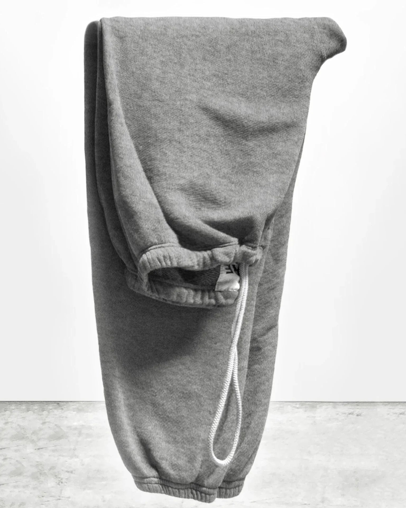 A pair of BASIC GOODNESS OG SWEATPANTS by Free City (sparrow, LLC) in gray French terry with an elastic waistband and white drawstring, neatly folded upright on a light gray textured surface against a plain white background.