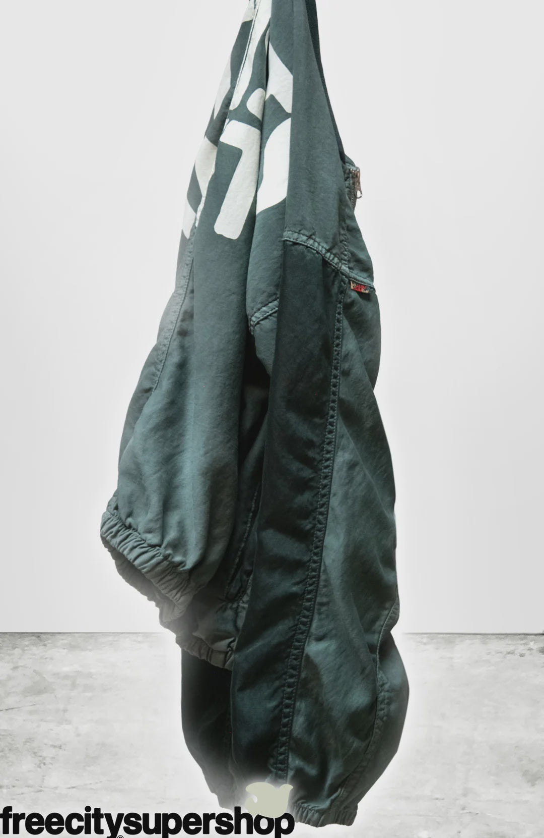 The Artist Wanted Matte Satin Air Jump Shell jogger pants by Free City (sparrow, LLC), handmade in Los Angeles with custom sunfade dye and elastic cuffs, hangs against a plain white background with "freecitysupershop" in black at the bottom left.