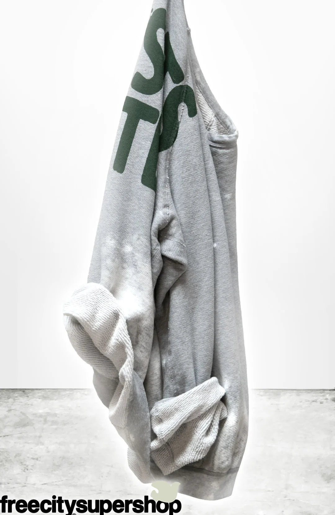 The A.W. Heather Bleachout Sweatshirt by Free City (sparrow, LLC) in light gray features hand-screen printed green partial text, white bleach-like spots, and "freecitysupershop" in black at the bottom, shown against a plain white background.