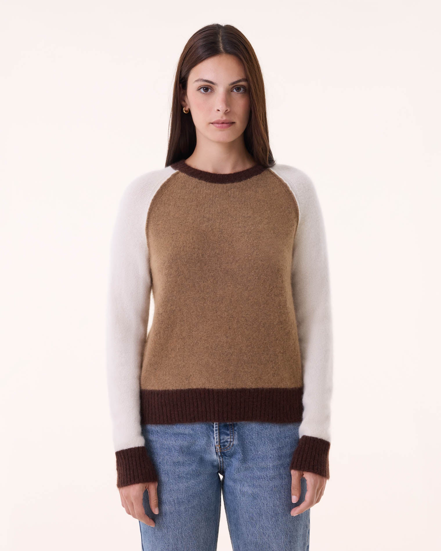 A woman with straight brown hair wears the BCS Group Nimbus Sweater—brown with white sleeves and dark brown cuffs—paired with blue jeans, standing against a plain light background.