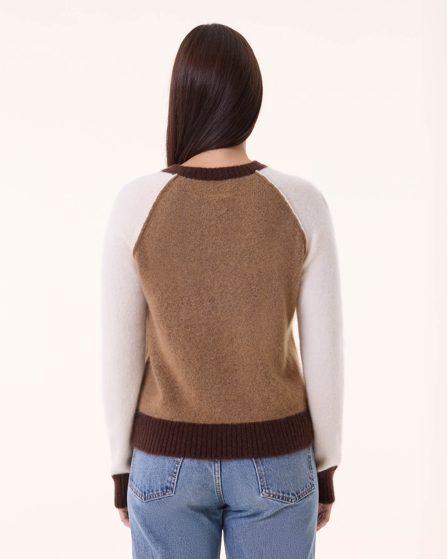 A person with long brown hair, seen from behind, wears the BCS Group Nimbus Sweater—brown with maroon cuffs and collar—paired with blue jeans, standing against a plain light background.